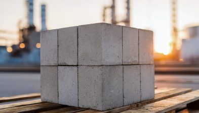 stack-solid-gray-concrete-blocks-arranged-wooden-pallet-with-industrial-factory-chimneys-blurred-background-sunset-light